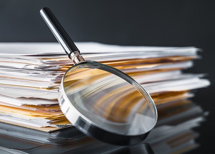 Image of a magnifying glass leaning against a stack of papers.