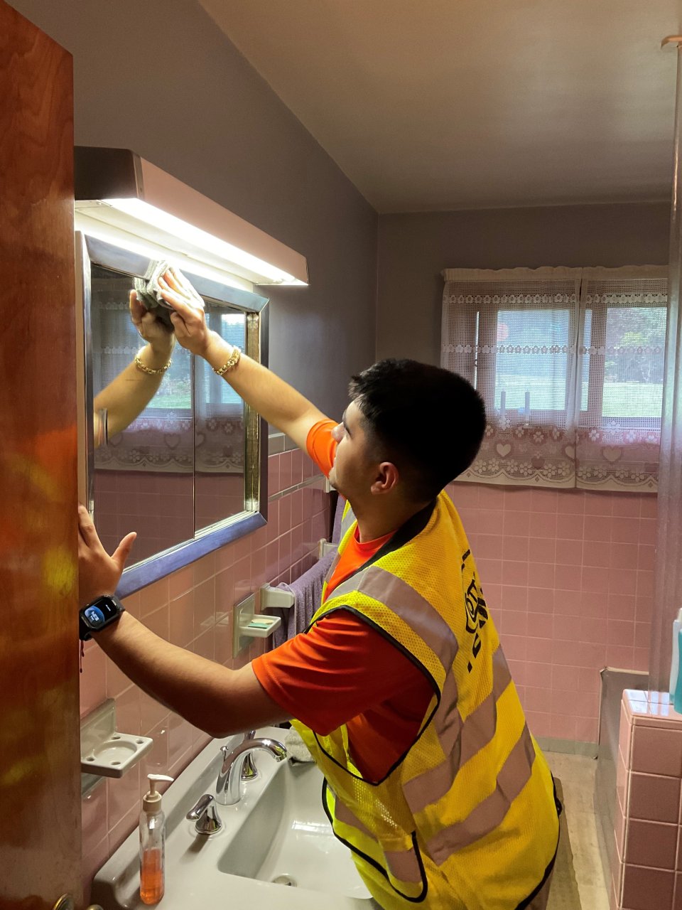 Man in worker vest cleaning a bathroom mirror