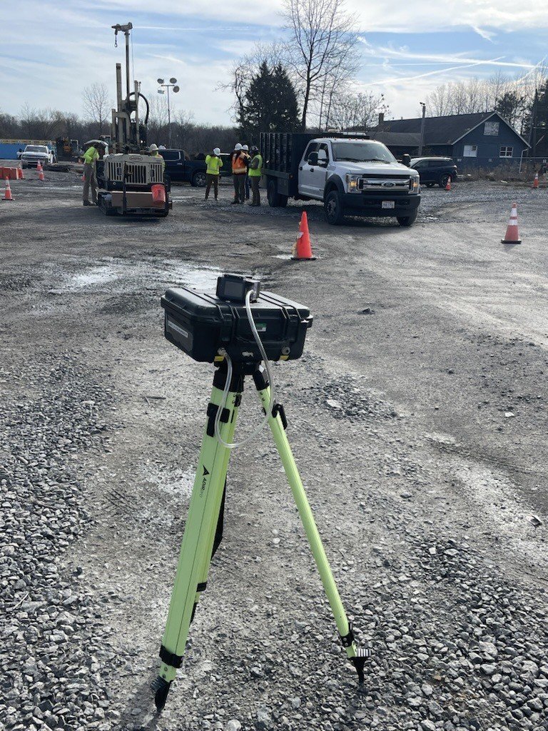 Air Sampling monitor set up on gravel with workers and trucks nearby.