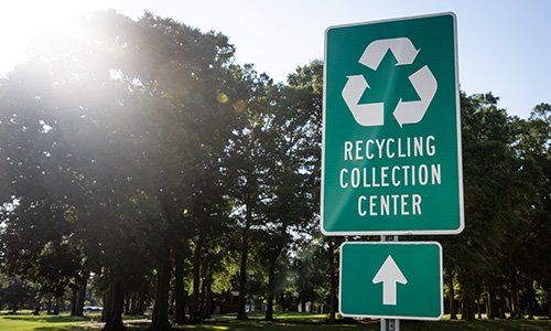 A sign in a park with trees. The sign reads, "Recycling Collection Center."