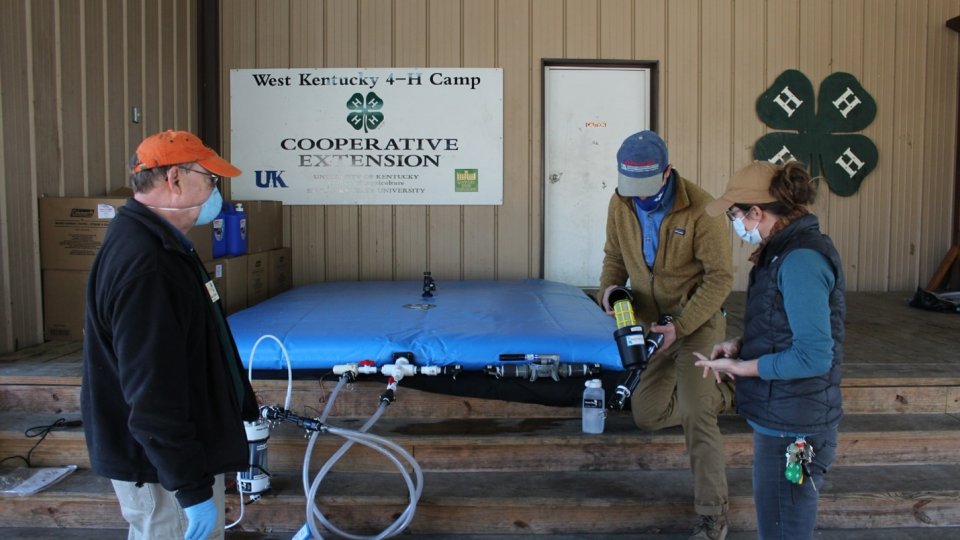Three people attending to a WOW Cart storage bladder, a big blue bag that stores treated water.