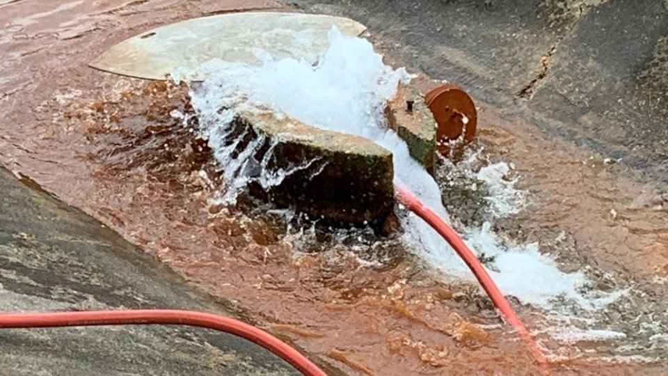 A red tube pumps air into a relief well. Water is bubbling and overflowing out of the top.