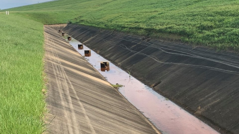 A row of relief wells poke up out of a concrete-lined ditch.