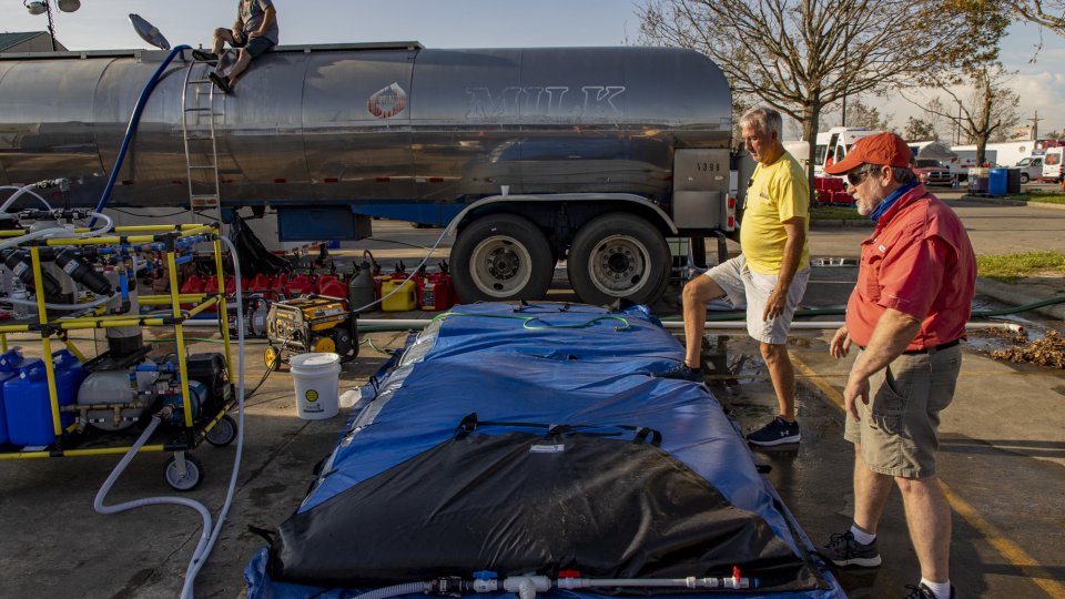 Two men attend to a blue bladder bag connected to the WOW Cart. A tanker truck sits behind them.