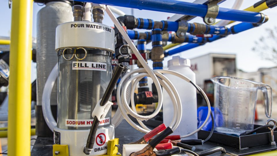 A closeup image of a chlorine gas generator on the WOW Cart. The generator is a small canister connected with tubing.