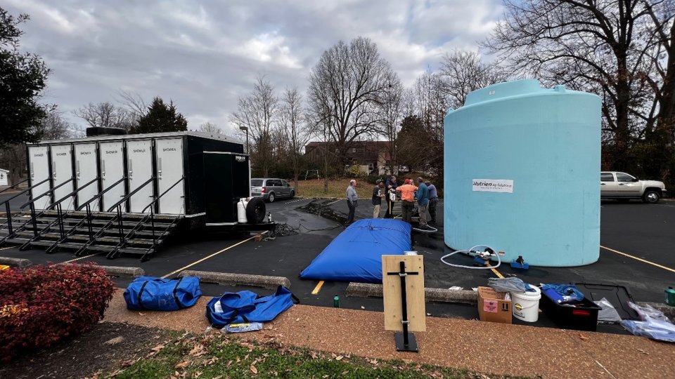 A parking lot staging area, showing a mobile shower trailer and a large storage container full of treated water.