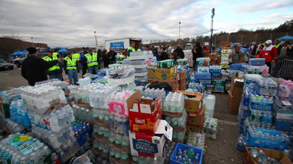 Stacks of hundreds of cases of bottled water in a parking lot staging area.