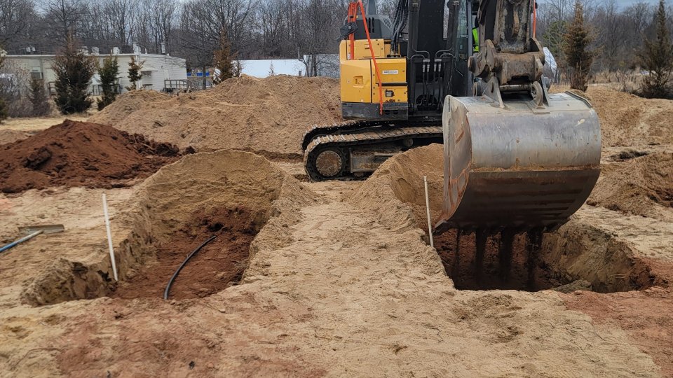 An excavator digs trenches in the dirt. Piles of dirt surround the excavator.