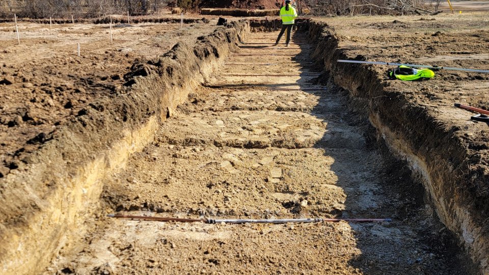 A trench dug in the ground, with sections of pipe laid in it.