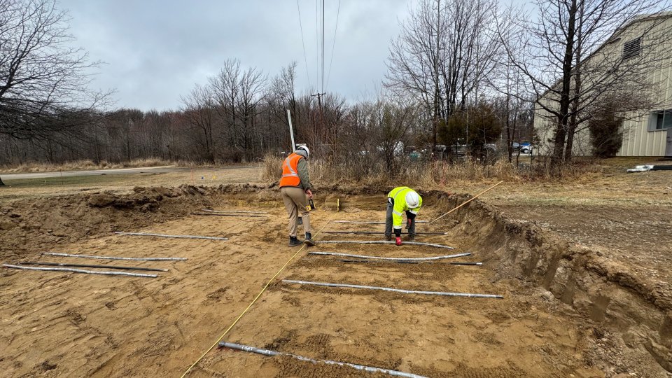 People in a shallow dirt trench, with sections of pipe laid along the ground.