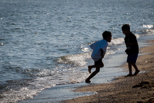 Two young boys playing on the beach next to the water