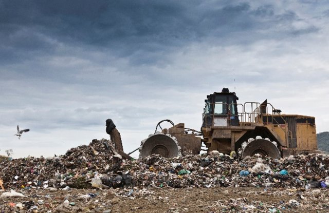 A large bulldozer pushing piles of trash at a landfill.