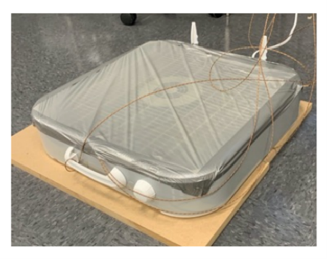 A box fan DIY air cleaner laying down horizontally with wires attached undergoing a safety test to assess fire and burn risks.