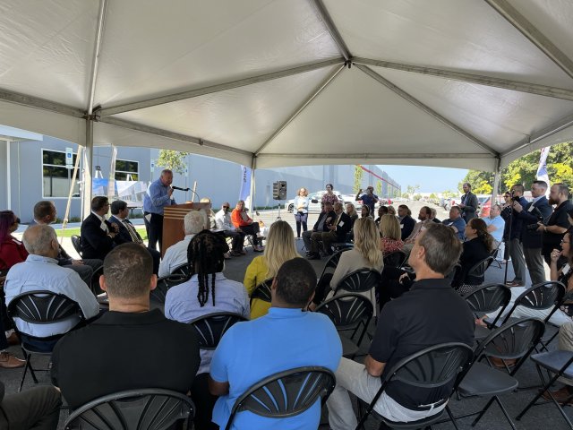 People sitting under a tent listening to a presentation by a speaker