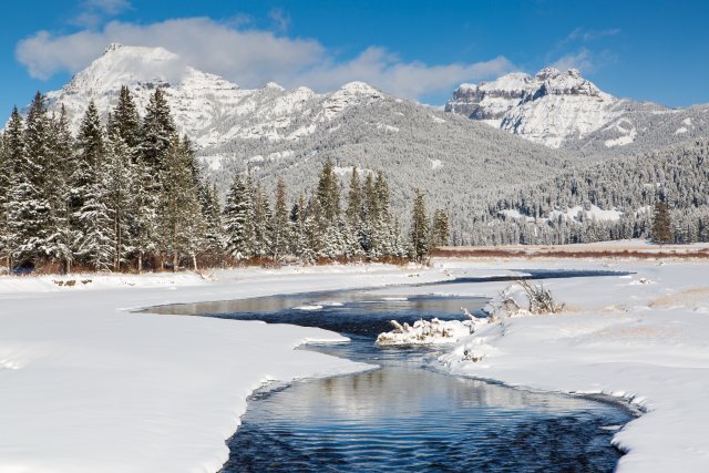 Snow covered landscape with stream flowing through and mountains in the distance.