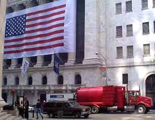Vacuum truck working in front of the New York Stock Exchange with a US flag hanging on the building.