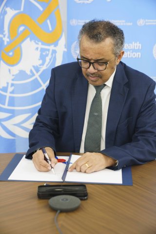 WHO Director-General Dr Tedros Adhanom Ghebreyesus signs the MOU in front of a WHO backdrop.