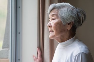 Older woman with silver hair looking out window.