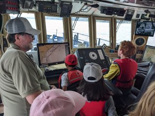 Lake Explorer II captain supervises as children sit in the captain's seat of the ship.