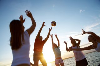 Photo of a group of young adults playing volleyball on a beach.