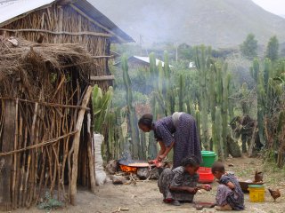 image of a woman cooking outside of a hut while two children play nearby