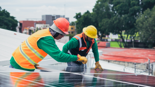 Two people in construction gear are working on a solar panel 