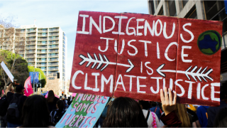 Person holding a red sign with white writing that says "Indigenous justice is climate justice" 