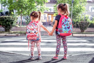 Two young children waiting at a crosswalk on their walk to school