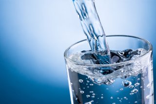 Clear glass being filled with water. Blue background 