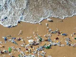 This is a picture of a beach with plastics waste strewn upon it and waves nearing the waste.