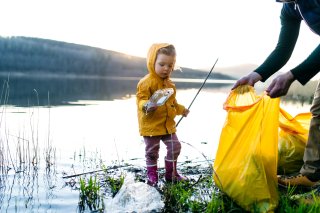 This is a photo of a young girl picking up plastic waste with an adult