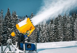 Yellow snow-making machine sprays snow onto a slope.