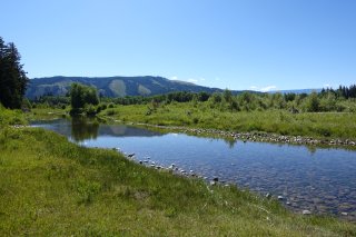 A calm river with grass on either side and a blue sky.