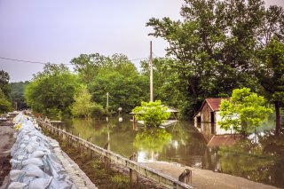 Flooded rural town with flooded trees and building. Row of sandbags on left.