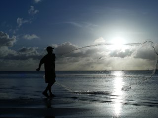 Silhouette of a man throwing a net out into the ocean.