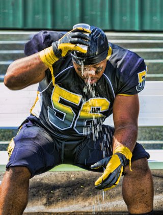 Seated football player in uniform pours water over his head.