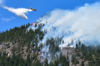 An airplane flies above a smoking hillside.