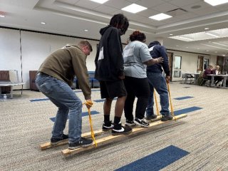 four people standing together on two boards, holding ropes