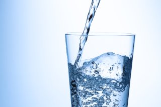 Water pouring into a clear glass of water against a blue backdrop.
