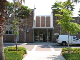 The front entrance to a large brick community center building. A white truck is parked in the foreground.