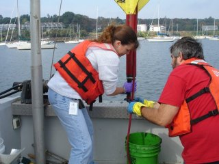 Two researchers in life vests on the water, collecting sediment samples