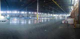 Sunlight from warehouse windows reflects off of a mostly-empty concrete floor inside of a cleaned-up former HPI facility.