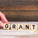 A hand places a letter g tile in the line of wooden letter tiles spelling grant