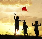 Three children flying a lite running in a field at sunset.