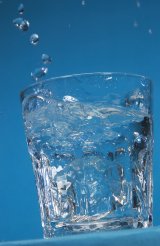 Glass being willed with water in front of a blue background
