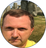 Lukas has dark hair and is wearing a yellow shirt while standing in front of a green field.