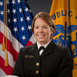 A smiling woman in a military uniform with short dark blonde hair.