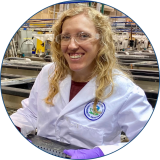 Speaker Chelsea Hintz has long blond curly hair and is wearing protective eyewear, a white jacket with the EPA logo on her left side, and purple gloves while holding samples at EPA's Experimental Stream Facility.