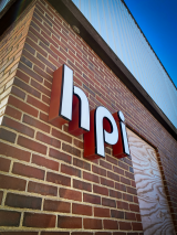 A brick building with a boarded-up door reads “hpi” in pop-out signage.